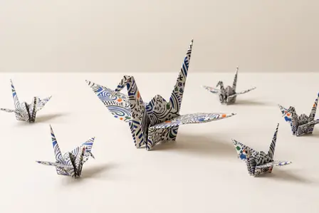 One large patterned origami crane surrounded by six smaller cranes folded from the same paper