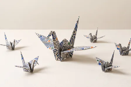 Um grande tsuru de origami estampado cercado por seis tsurus menores dobrados com o mesmo papel